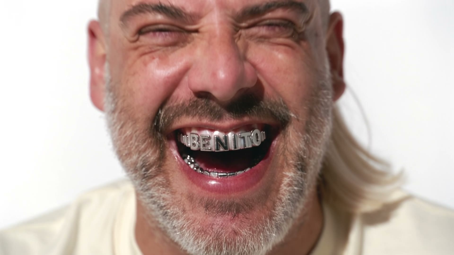 Benito laughing in close-up, silver grillz reading BENITO