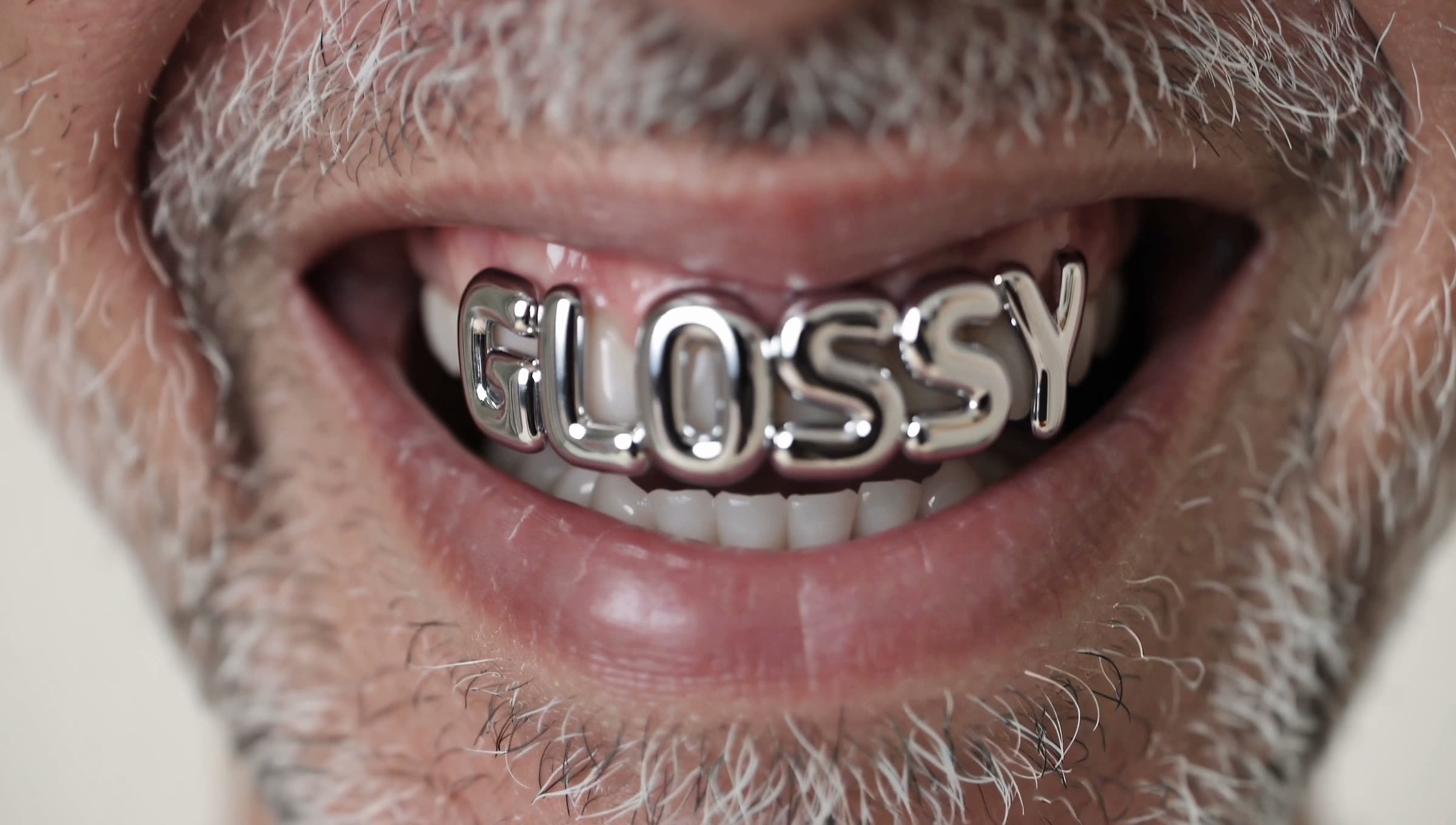 Macro of a laughing mouth with chrome grillz spelling GLOSSY